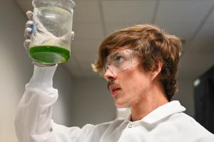 UTC Graduate Student UTC science student looking at a beaker wearing goggles
